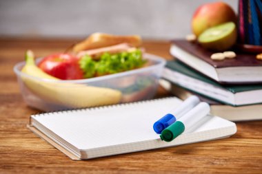 Okul öğle yemeği molası ile sağlıklı öğle yemeği kutusu ve okul malzemeleri ahşap masa, seçici odak kavramı.