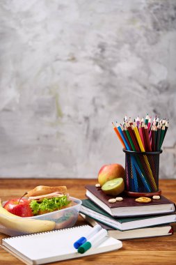 Okul öğle yemeği molası ile sağlıklı öğle yemeği kutusu ve okul malzemeleri ahşap masa, seçici odak kavramı.