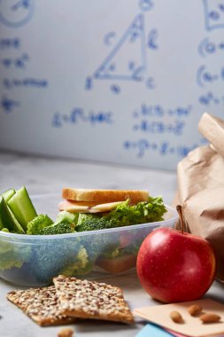 Geri okul kavramı, okul malzemeleri, bisküvi, paket öğle yemeği ve beslenme çantası beyaz yazı tahtası, seçici odak üzerinde.