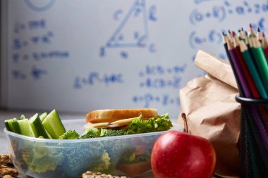 Geri okul kavramı, okul malzemeleri, bisküvi, paket öğle yemeği ve beslenme çantası beyaz yazı tahtası, seçici odak üzerinde.