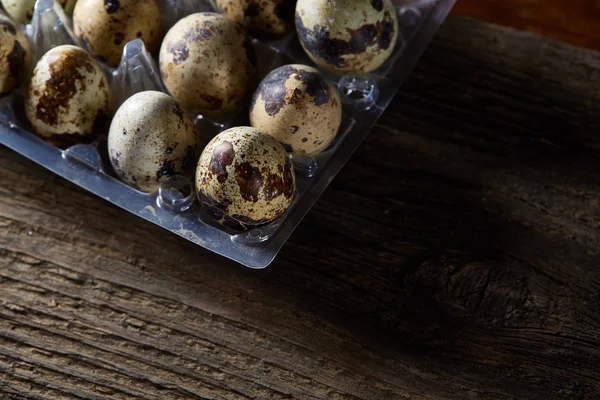 stock image Quail eggs in a plastic container on a dark wooden background, top view, selective focus, shallow depth of field