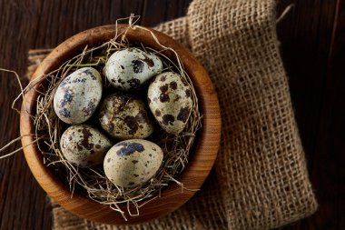 Koyu ahşap arka plan, üstten görünüm, yakın çekim saf peçeteye ahşap bir kase taze bıldırcın yumurtası