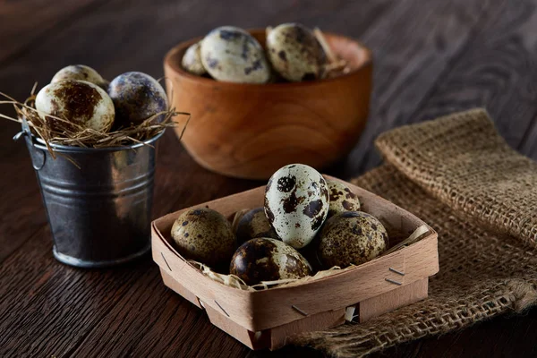 Rustic still life with quail eggs in bucket, box and bowl on a linen napkin over wooden background, selective focus — Stock Photo, Image