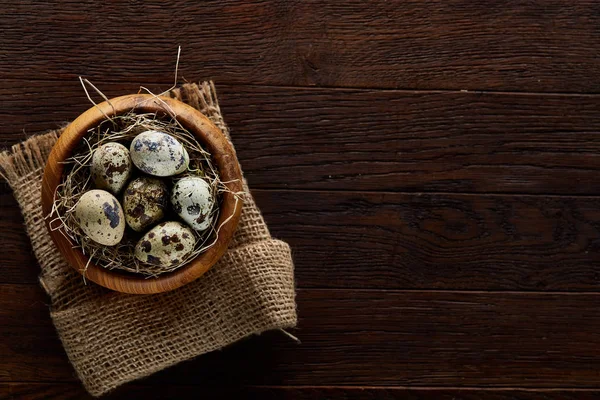 Huevos frescos de codorniz en un tazón de madera en una servilleta hecha en casa sobre fondo de madera oscura, vista superior, primer plano — Foto de Stock