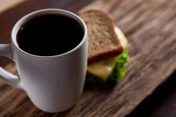 Breakfast table with sandwich and black coffee on rustic wooden background, close-up, selective focus — Stock Photo, Image