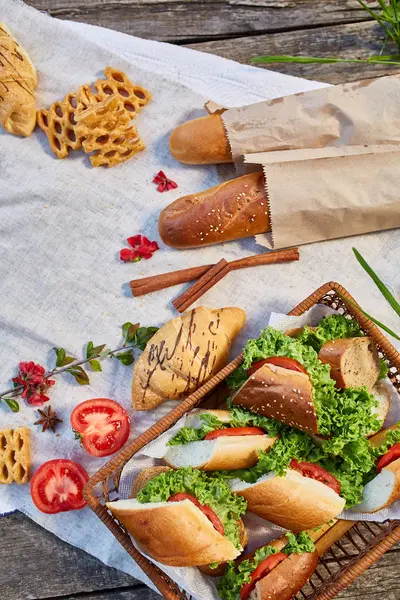 Cesta de picnic llena de sándwiches, baguette y croissant en un mantel hecho en casa, puesta plana, enfoque selectivo — Foto de Stock