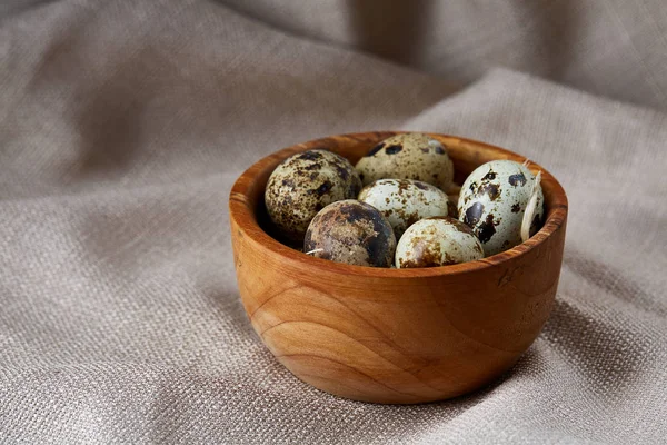 Quail eggs in a wooden bowl on a homespun tablecloth, top view, close-up — Stock Photo, Image