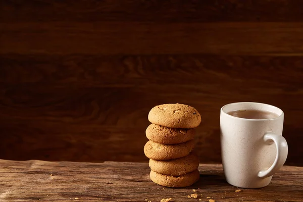 White porcelain mug of tea and sweet cookies on piece of wood over wooden background, top view, selective focus — Stock Photo, Image