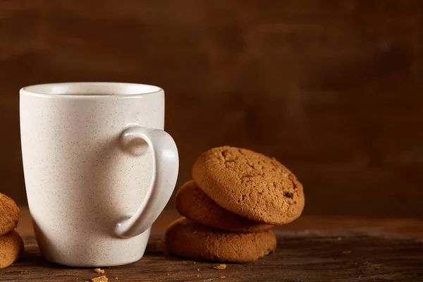 Caneca de porcelana branca de chá e biscoitos doces em pedaço de madeira sobre fundo de madeira, vista superior, foco seletivo — Fotografia de Stock