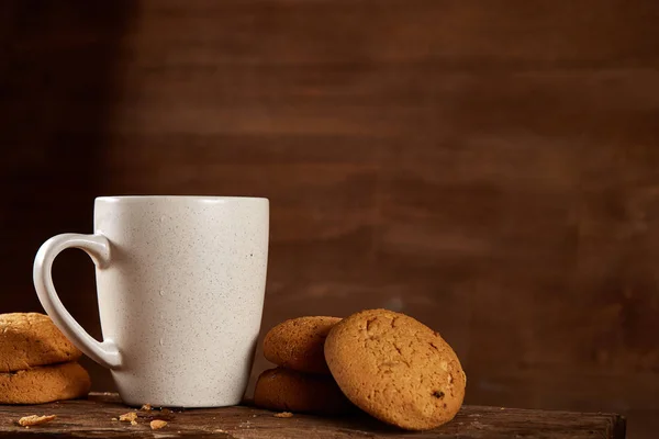 White porcelain mug of tea and sweet cookies on piece of wood over wooden background, top view, selective focus — Stock Photo, Image