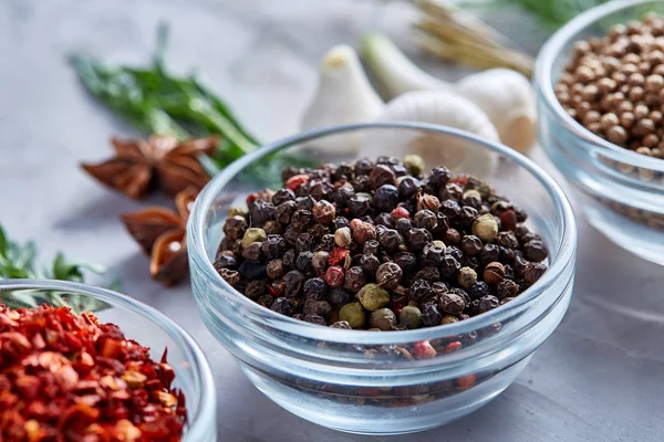 Transparent glass bowls with peppercorns and dried chilly among exotic spicies, close-up, top view, selective focus.