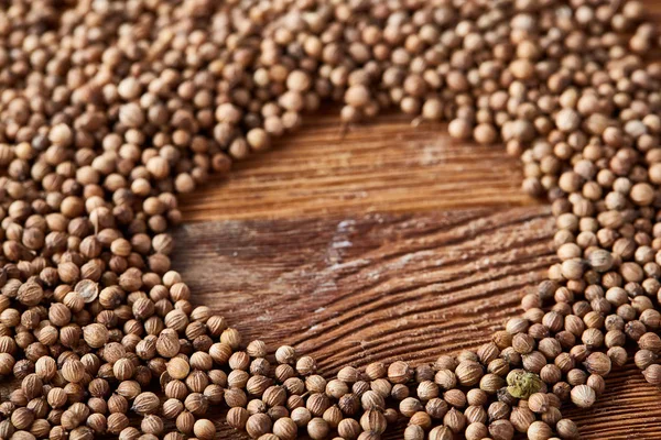 Circle frame made of coriander seeds on the rustic wooden background, close-up, top view, macro, selective focus.