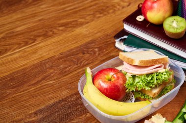 Okul veya sandviç ile öğle yemeği kutusu ve çeşitli renkli sebze ve meyve ahşap arka plan üzerinde piknik, yakın çekim.