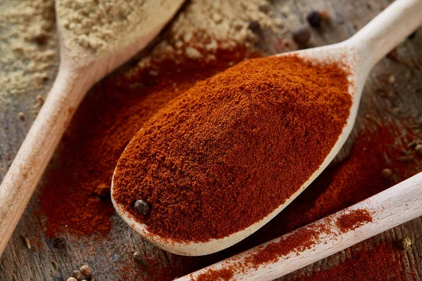 Draufsicht auf einen Holzlöffel voll Paprika und schwarzem Pfeffer auf hölzernem Fasshintergrund, selektiver Fokus. — Stockfoto