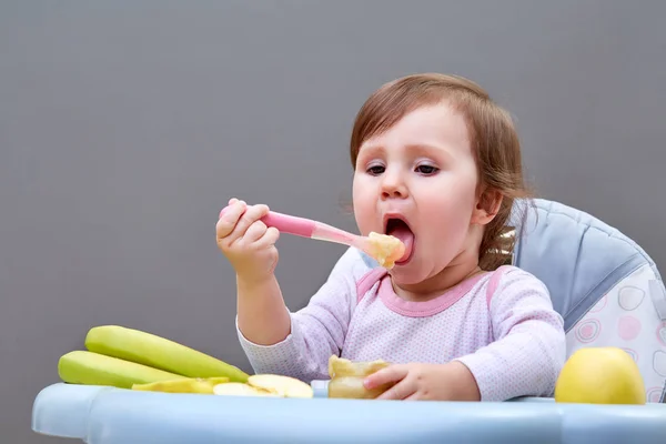 Adorable toddler girl is having fun while eating some fruits on greyish background — Stock Photo, Image