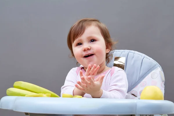 Menina da criança adorável está se divertindo enquanto come algumas frutas em fundo acinzentado — Fotografia de Stock