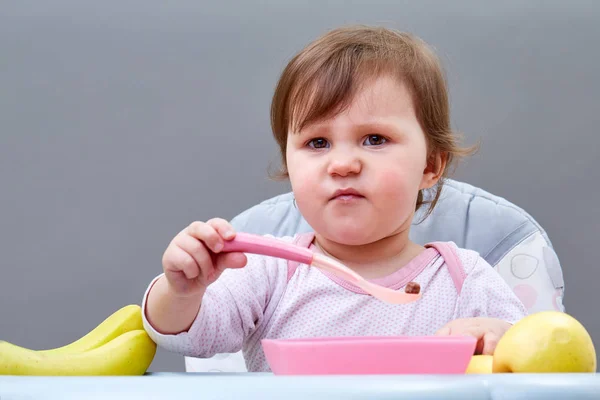 Очаровательная девочка малыша получает удовольствие во время еды некоторые фрукты на сероватом фоне — стоковое фото