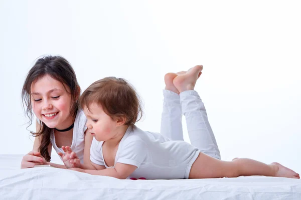 Dos hermanas jugando juntas en juegos en el teléfono inteligente en fondo blanco estudio . — Foto de Stock