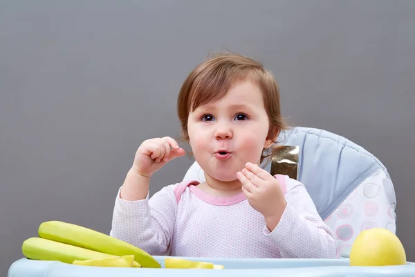 사랑 스러운 유아 소녀 회색 배경에 일부 과일을 먹는 동안 재미는 — 스톡 사진
