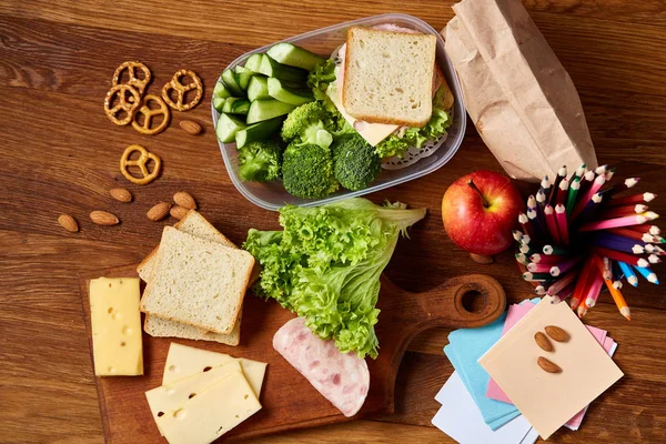 Okul öğle yemeği molası ile sağlıklı öğle yemeği kutusu ve okul malzemeleri ahşap masa, seçici odak kavramı.