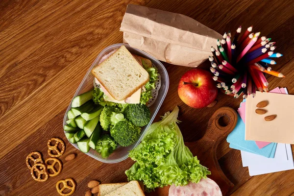 Okul öğle yemeği molası ile sağlıklı öğle yemeği kutusu ve okul malzemeleri ahşap masa, seçici odak kavramı.