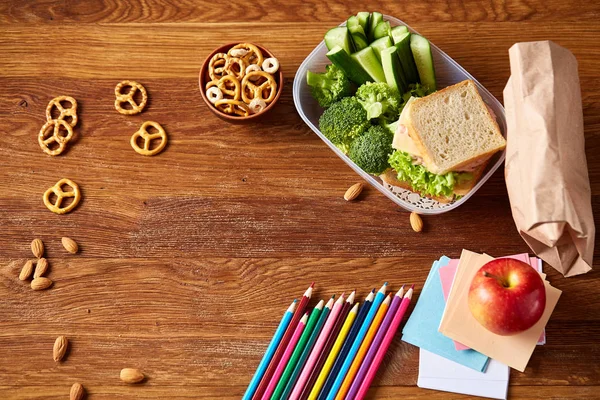 Okul öğle yemeği molası ile sağlıklı öğle yemeği kutusu ve okul malzemeleri ahşap masa, seçici odak kavramı.