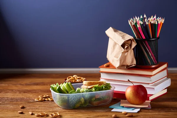Concept of school lunch break with healthy lunch box and school supplies on white desk, selective focus.