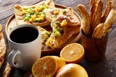 Sabah bir fincan kahve, breadsticks, meyve pasta ve ahşap zemin üzerine portakal konseptiyle.