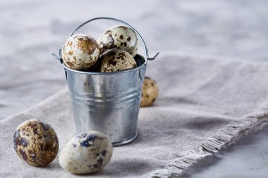 Küçük dekoratif kova peçete bıldırcın yumurtalarının dolu beyaz dokulu arka plan, yakın çekim, seçici odak üzerinde.