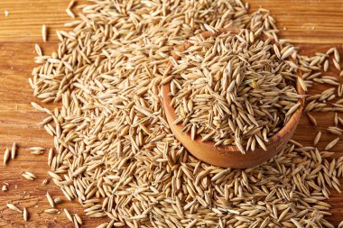 Ahşap arka plan, üstten görünüm, yakın çekim, makro, sığ derinlik-in tarla soyulmamış yulaf taneleri yığını.