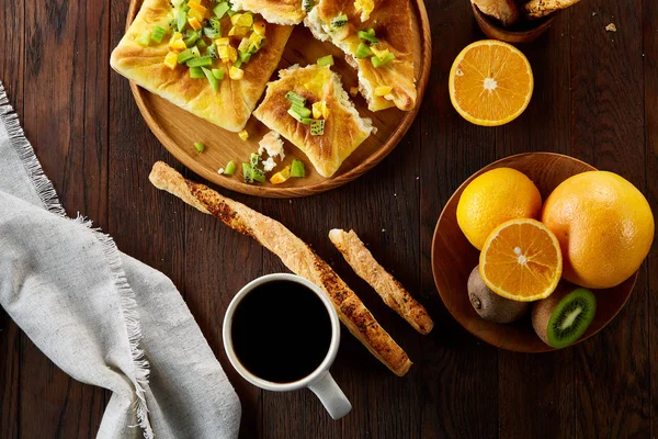 Sabah bir fincan kahve, breadsticks, meyve pasta ve ahşap zemin üzerine portakal konseptiyle.