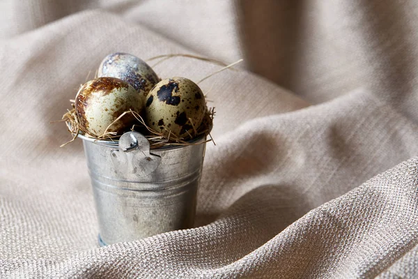 Pequeño cubo decorativo lleno de huevos de codorniz en servilleta sobre fondo de textura blanca, primer plano, enfoque selectivo . — Foto de Stock