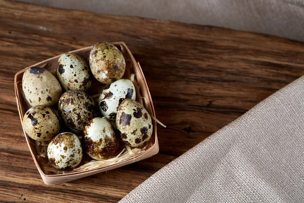Quail eggs in the container on piece of wood over homespun tablecloth, close-up, high angle view, selective focus. — Stock Photo, Image
