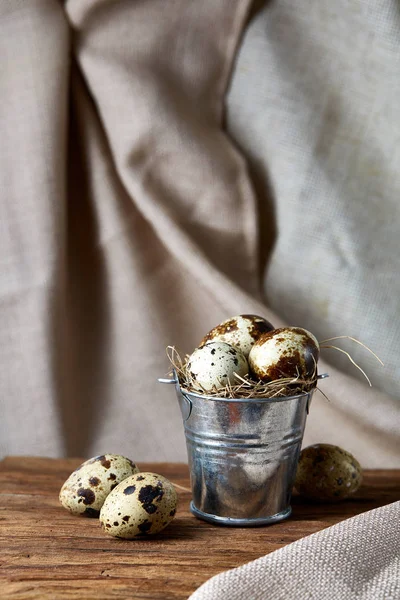 Bıldırcın yumurtası odun parçası üzerinde küçük dekoratif kova dolu saf masa örtüsü, yakın çekim, seçici odak üzerinde.
