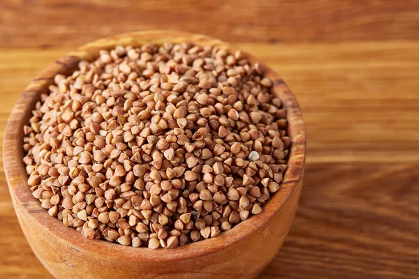 Bowl full of buckwheat grains on rustic wooden table, close-up, selective focus, shallow depth of field.