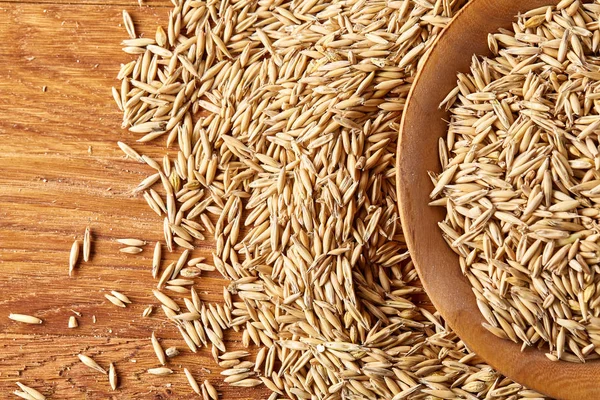 Ahşap arka plan, üstten görünüm, yakın çekim, makro, sığ derinlik-in tarla soyulmamış yulaf taneleri yığını.