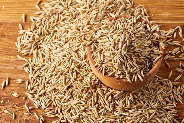 Ahşap arka plan, üstten görünüm, yakın çekim, makro, sığ derinlik-in tarla soyulmamış yulaf taneleri yığını.