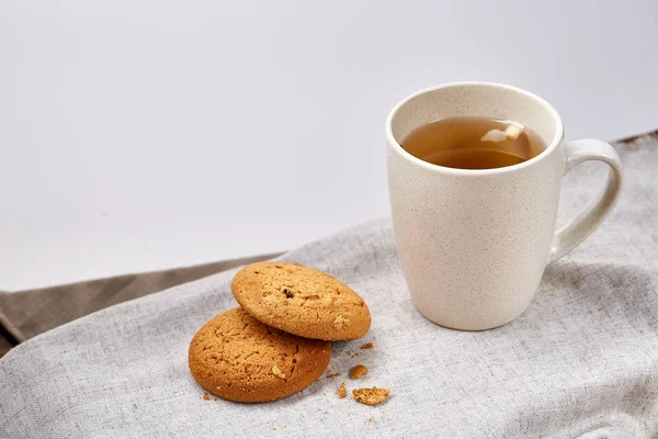 Taza de porcelana blanca de té y galletas dulces en servilleta casera sobre fondo blanco, vista superior, enfoque selectivo — Foto de Stock