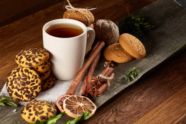 Concepto de Navidad con una taza de té caliente, galletas y decoraciones en un registro sobre fondo de madera, enfoque selectivo —  Fotos de Stock