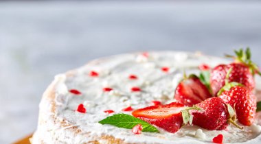 Çilek ve beyaz dokulu arka planda, seçici odak nane yaprakları ile süslenmiş krem şanti ile tart