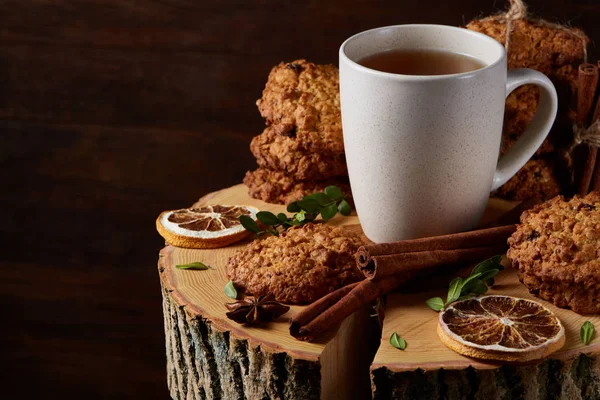 Weihnachtskonzept mit einer Tasse heißem Tee, Plätzchen und Dekorationen auf einem Baumstamm über Holzgrund, selektiver Fokus — Stockfoto