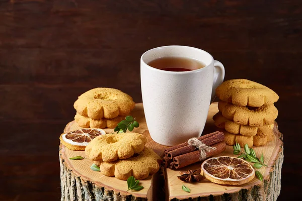 Christmas concept with a cup of hot tea, cookies and decorations on a log over wooden background, selective focus — Stock Photo, Image