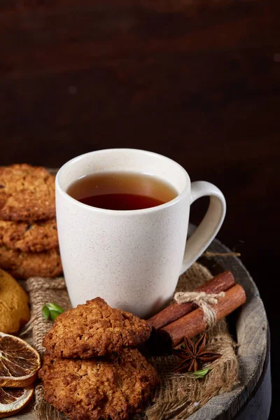 Conceptual festive composition with a cup of hot tea, cookies and spicies on a wooden barrel, selective focus, close-up