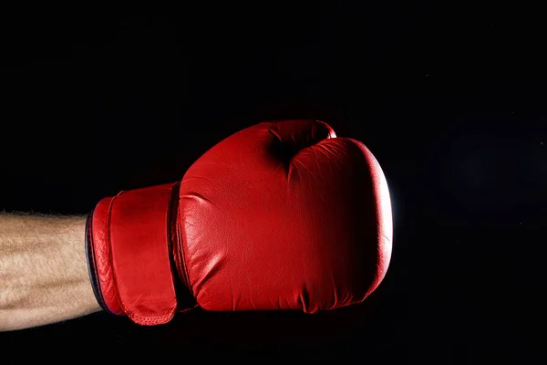 A fighters red boxing gloves on his hand isolated on dark blurred background, close-up.