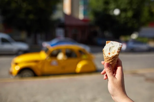 A first person view, a person walking along the road with an ice cream in his hands, shallow depth of field.
