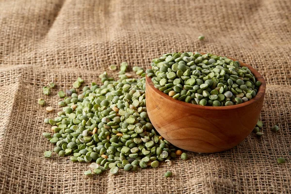 Organic green peas in a bowl on burlap tablecloth, close-up, top view, selective focus. — Stock Photo, Image