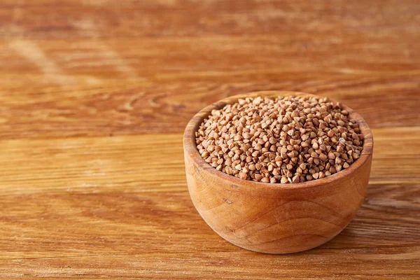 Bowl full of buckwheat grains on rustic wooden table, close-up, selective focus, shallow depth of field.