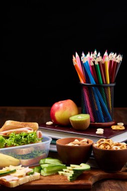 Okul öğle yemeği molası ile sağlıklı öğle yemeği kutusu ve okul malzemeleri ahşap masa, seçici odak kavramı.