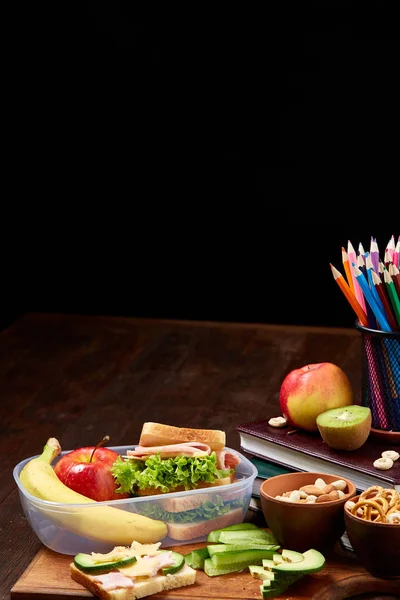 Okul öğle yemeği molası ile sağlıklı öğle yemeği kutusu ve okul malzemeleri ahşap masa, seçici odak kavramı.