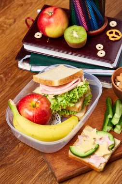 Okul öğle yemeği molası ile sağlıklı öğle yemeği kutusu ve okul malzemeleri ahşap masa, seçici odak kavramı.
